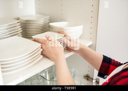 Frau legt sauberes Geschirr auf dem Regal im Küchenschrank. Stockfoto