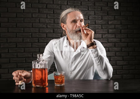Ältere Menschen trinken Whisky und Zigarre rauchen auf dunklem Hintergrund Stockfoto