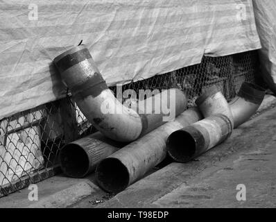 Nahaufnahme von beschädigten Rohren aus Metall auf Betonboden, Monochrom Stockfoto