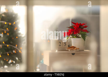 Weihnachtsstern Weihnachtsstern mit Plätzchen und ein Glas Milch auf hölzernen Tisch Stockfoto