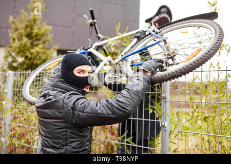 Zwei Fahrräder Diebe stehlen ein Fahrrad und es über einen Zaun heben Stockfoto