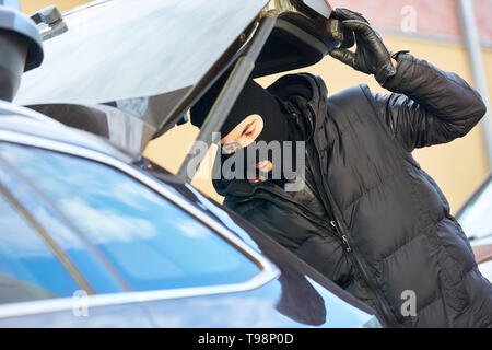 Dieb mit Balaclava öffnet Koffferraum eines Autos Stockfoto