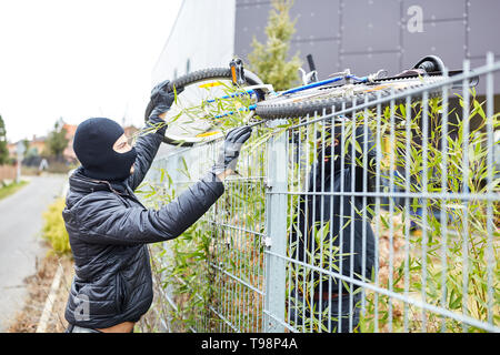 Zwei Diebe stehlen ein Fahrrad und es über einen Zaun während der Diebstahl von Fahrrädern Stockfoto