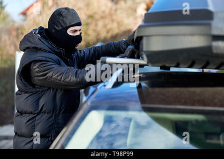 Dieb öffnet Dachbox oder Dachgepäckträger auf ein Auto für Diebstahl Stockfoto