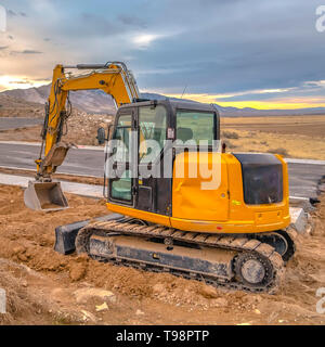 Bagger auf der Seite der Straße gegen eine zerklüftete Berge und Dramatischer Himmel Stockfoto