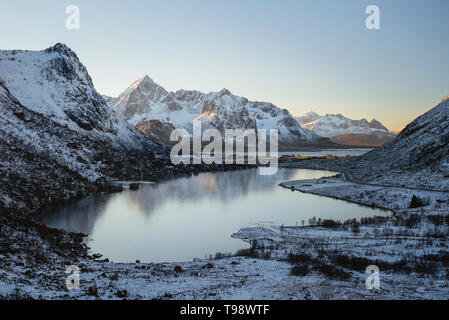 Gefrorenen See spiegelt den sonnenbeschienenen Gipfel der Berge im Hintergrund, Lofoten, Nordland, Norwegen Stockfoto