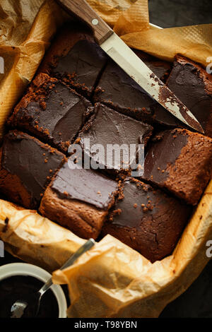 Leckere frisch gebackene Gesund vegan Feucht dark chocolate brownies Dessert oder Kuchen mit Kaffee bereifen Schnitt in Quadrate auf Backpapier Draufsicht Stockfoto