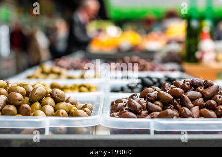 Sortiment von Oliven auf dem Markt. Reihen von verschiedenen Arten von Oliven in transparentem Kunststoff Schalen. Verschwommen Kunden für den Hintergrund. Stockfoto