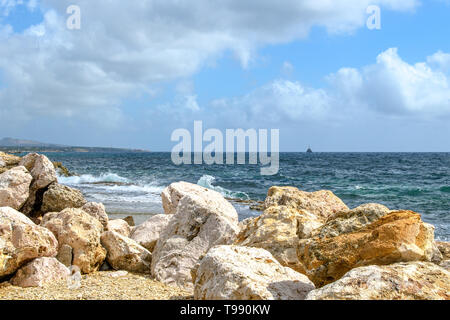 Meereslandschaft mit riesigen Felsen im Vordergrund, Surf Wellen, Schiff Silhouette am Horizont und blauer Himmel mit Wolken. Stockfoto