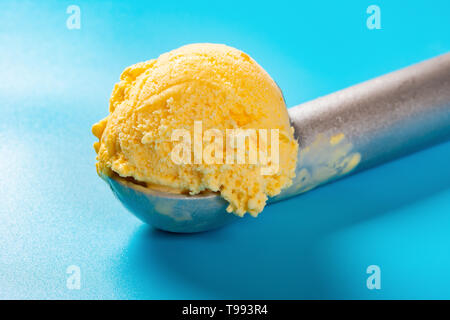 Löffel mit Mango geschmack Eis Ball auf blauem Hintergrund Nahaufnahme Stockfoto