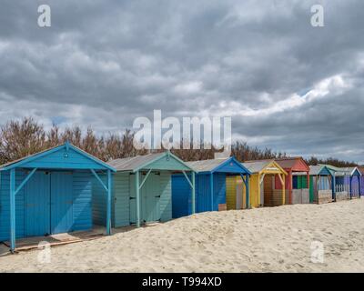 Eine Reihe von bunten hölzernen Umkleidekabinen am Strand an einem Sandstrand im Süden von England an einem bewölkten Tag Stockfoto