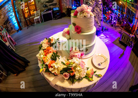 Hochzeitstorte mit Blumen auf dem Tisch eingerichtet. Drei abgestufte Hochzeitstorte und Platte mit Gabel auf weißer Tisch. Aufnahme mit Fischaugenobjektiv. Stockfoto