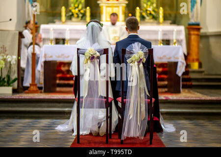 Braut und Bräutigam während der Trauung in der Kirche. Braut und Bräutigam Vorbereitung der Gemeinschaft auf die Knie bei der Trauung in der Kirche. Lehrstühle wi eingerichtet Stockfoto
