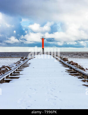 Orange Rundumleuchte auf einem schneebedeckten Wellenbrecher in der Ostsee, Lettland. Stockfoto