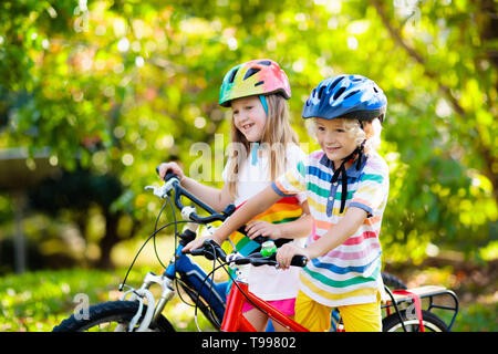 Kids on Bike im Park. Kinder in die Schule zu tragen sichere fahrradhelme. Kleine Jungen und Mädchen Radfahren auf sonnigen Sommertag. Aktiv gesund Outdoor sp Stockfoto