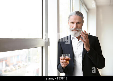 Ältere Menschen trinken Whisky und Zigarre rauchen in der Nähe der Fenster Stockfoto