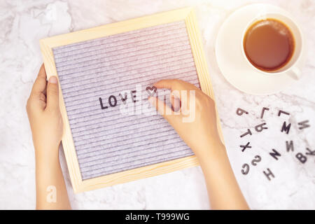 Wort Liebe auf Brief mit der Frau Hand Herz Symbol auf weißem Marmor Schreibtisch Hintergrund mit Kaffeetasse Stockfoto