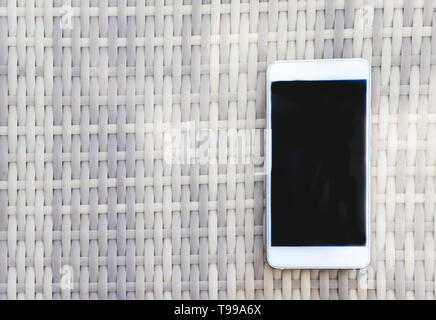 White Smartphone liegt auf einer Rattan Tisch im Freien. Ansicht von oben Stockfoto