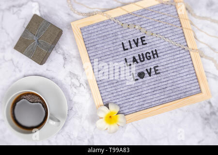 Wort Live Laugh Love letter Board auf weißem Marmor Schreibtisch Hintergrund mit Kaffeetasse und Geschenkbox, Dekoration mit Blumen- und Luxury Pink Halskette