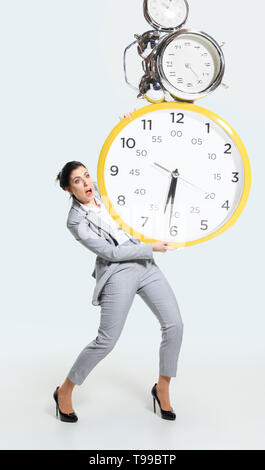 Junge Frau kann ihre Arbeitszeit nicht organisieren. Gezwungen, ständig zu bleiben und länger arbeiten. Die große Uhr, hat keine Zeit. Konzept der Probleme im Büro, Geschäft oder Probleme mit der psychischen Gesundheit. Stockfoto