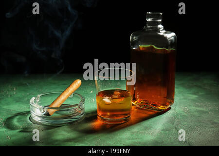 Flasche und Glas Whiskey mit Zigarre auf Farbtabelle gegen den dunklen Hintergrund Stockfoto