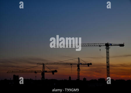 Baukraene waerend der blauen Stunde vor dem Abendhimmel der sich von rot nach blau Faerbt. Stockfoto