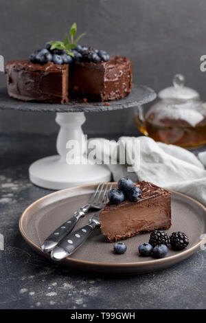 Stück Schokolade Kuchen mit ganzen Kuchen hinter auf grauem Hintergrund. Konzept der süßen Urlaub essen. Seitenansicht Stockfoto