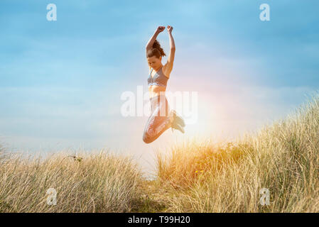 Sportliche Frau laufen und springen in den Sanddünen, gesund und glücklich, springen vor Freude. Stockfoto