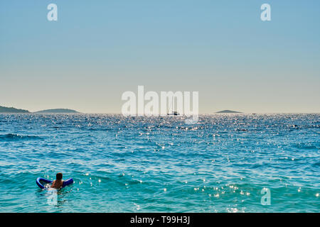 Man schwimmt auf Luftmatratze, auf dem Segelboot in der Ferne in Sibenik, Dalmatien, Kroatien Suche Stockfoto