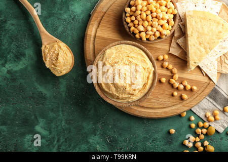 Schüsseln und Löffel mit Hummus auf Farbtabelle Stockfoto