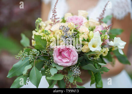 Kaukasische junge Braut Tragen eines weißen, Lacy Kleid und mit einem schönen Brautstrauß von Rosen und gemischten Sommer Blumen und Grün Stockfoto