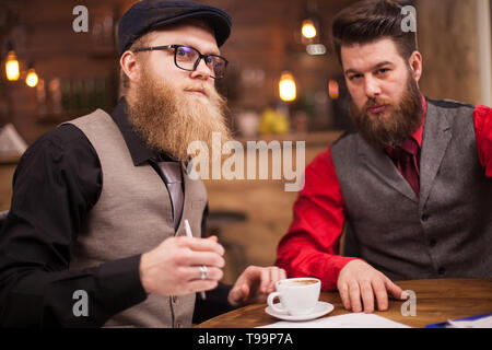 Zwei erfolgreiche Geschäftsleute in einer wichtigen Sitzung in vintage Pub. Kaffeetasse. Attraktive Männer. Teamarbeit. Stockfoto