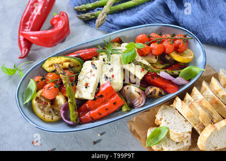 Gegrilltes Mediterranes Gemüse mit warmem Schafskäse serviert auf einem blauen Keramikplatte auf eine Tabelle mit konkreten Aussehen Stockfoto