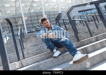 Junge afrikanische amerikanische Mann sitzt auf der Treppe auf der Stadt Straße Kamera lächelt zuversichtlich Stockfoto