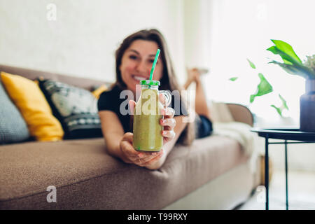 Glückliche junge Frau, die sich in Wohnzimmer und trink Smoothie. Gesunde Ernährung Stockfoto