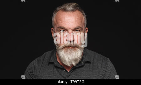 Der Mann mit dem weißen Bart an der Kamera schaut. Portrait eines älteren Mannes auf schwarzen Hintergrund isoliert. Stockfoto