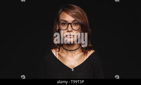 Frau in Brillen auf schwarzem Hintergrund isoliert. Porträt einer modischen Frau mit durchbohrten Lippen an Kamera schaut. Stockfoto