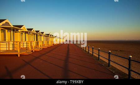 Am frühen Abend Sunshine auf die Schmiedearbeiten Geländer am Meer wirft einen langen Schatten in der Mitte der Promenade vor der St Annes Strandhütten Stockfoto