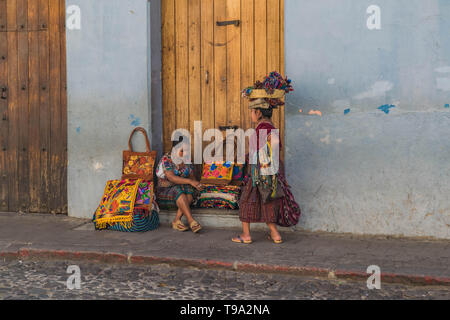 Zwei Frauen Straßenhändler in traditioneller Kleidung, eine mit einem Korb auf dem Kopf, Verkauf von guatemaltekischen Güter auf einer Straße mit Kopfsteinpflaster in Antigua Guatemala Stockfoto