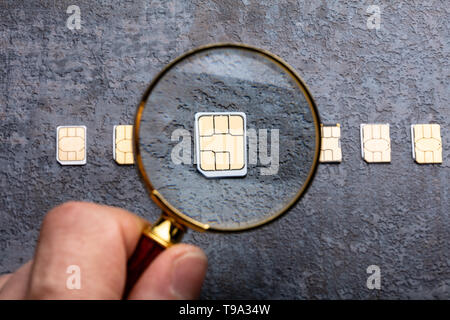 Person's Hand mit Lupe über Nano-SIM-Karte auf rauen Hintergrund Stockfoto