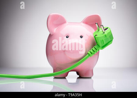 Green Power Plug und rosa Sparschwein auf reflektierenden Schreibtisch Stockfoto