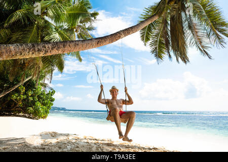 Glückliche junge Mann genießen Schwingen auf dem idyllischen Strand Stockfoto