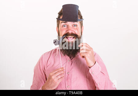 Hipster mit Bart und Schnurrbart auf glücklich mit Photo Booth Requisiten posieren. Guy raucht Tabakpfeife. Aristokratie Konzept. Mann hält Papier Partei Requisiten Tabakpfeife und Hut, weißen Hintergrund. Stockfoto