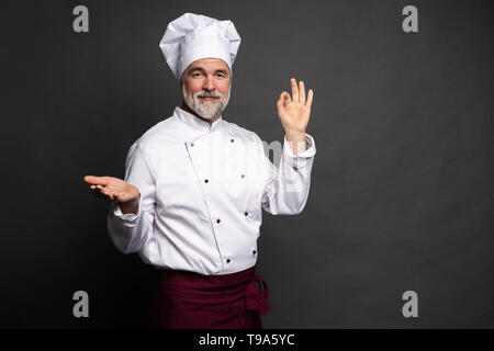 Koch, lecker lecker Geste durch Küssen Finger. Zuversichtlich bärtigen Mann Koch in weiße Uniform mit perfekter unterzeichnen. Stockfoto