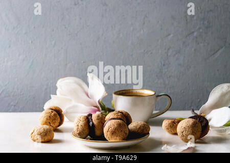 Baci di dama hausgemachte italienische Haselnuss Kekse Kekse mit Schokolade in Keramik Platte mit Tasse Espresso und Magnolia Blumen serviert. Stockfoto