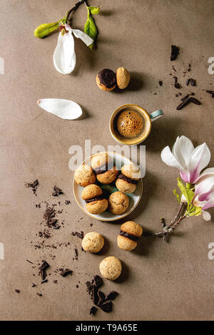 Baci di dama hausgemachte italienische Haselnuss Kekse Kekse mit Schokolade in Keramik Platte mit Tasse Espresso und Magnolia Blumen serviert. Stockfoto