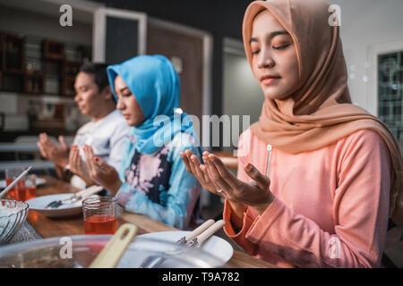 Hijab Frauen und ein Mann zusammen beten vor dem Essen, eine schnelle brechen Mahlzeit auf einem Tisch im Garten serviert. Stockfoto