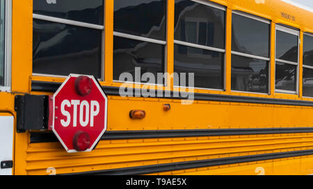 Klar Panorama Seitenansicht eines School Bus auf einer Straße, die durch verschneite Häuser im Winter Stockfoto