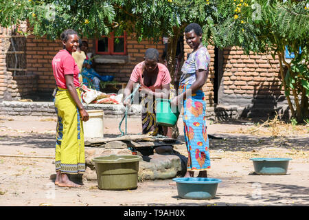Malawische Frauen Zeichnung Wasser in der Mittagssonne aus einem flachen Brunnen in einem Dorf mit Plastikeimer und Seil Stockfoto