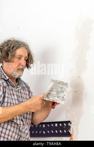 Builder Reparatur eines Risses in der Wand mischen Gips auf einem Handheld Platte mit einem Spachtel bereit die Einrichtung berührt, an die Oberfläche zu gelten, Fokus zu t Stockfoto